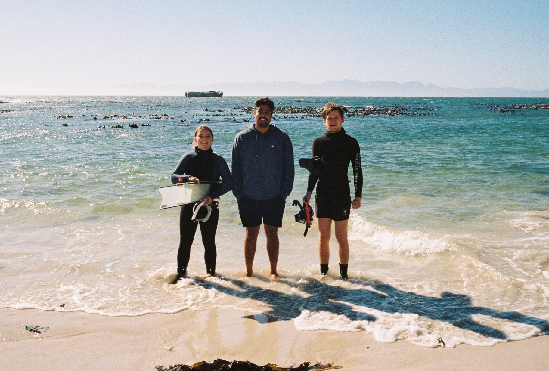 Three of the crew standing in the shallows with kelp behind them