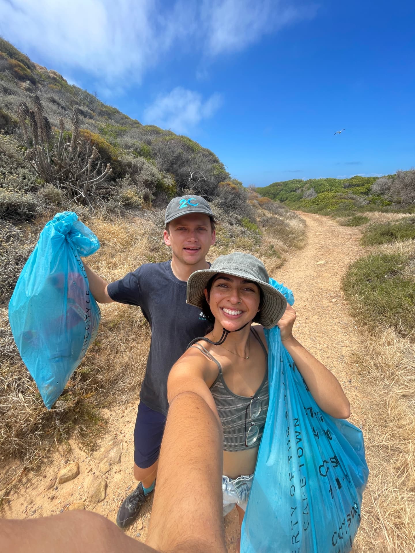 Two volunteers holding bags of collected trash on the trail